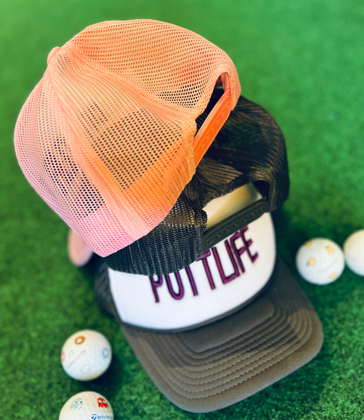 Putt Life Golf foam trucker hat—pink brim and pink mesh, white front with ‘PUTTLIFE’ in purple in the grass with golf ball in the background snapback back view.