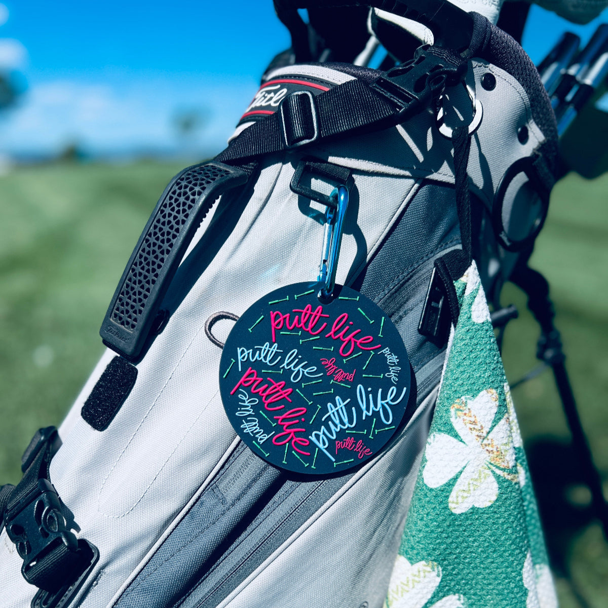 Putt Life Golf navy blue putting disc with pink and light blue putt life logos and neon green putters on it, attached to a golf bag