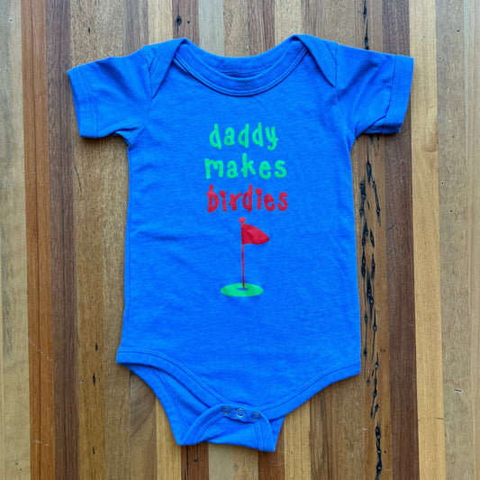 Putt Life Golf blue baby onesie with the text 'Daddy makes birdies' and a green and red golf green and flag graphic on the front 1Z