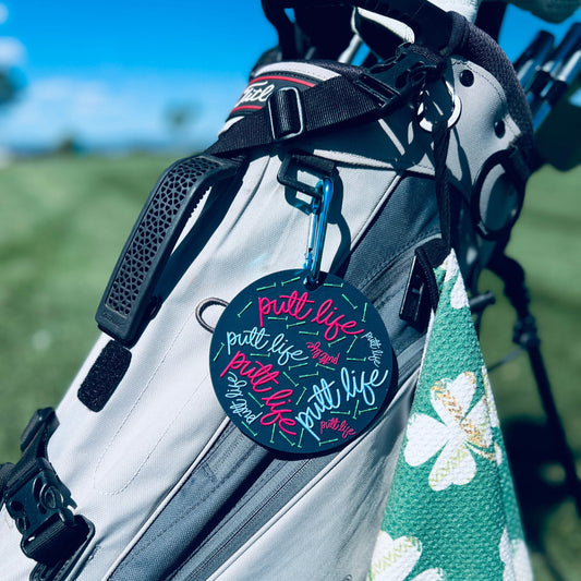 Putt Life Golf navy blue putting disc with pink and light blue putt life logos and neon green putters on it, attached to a golf bag